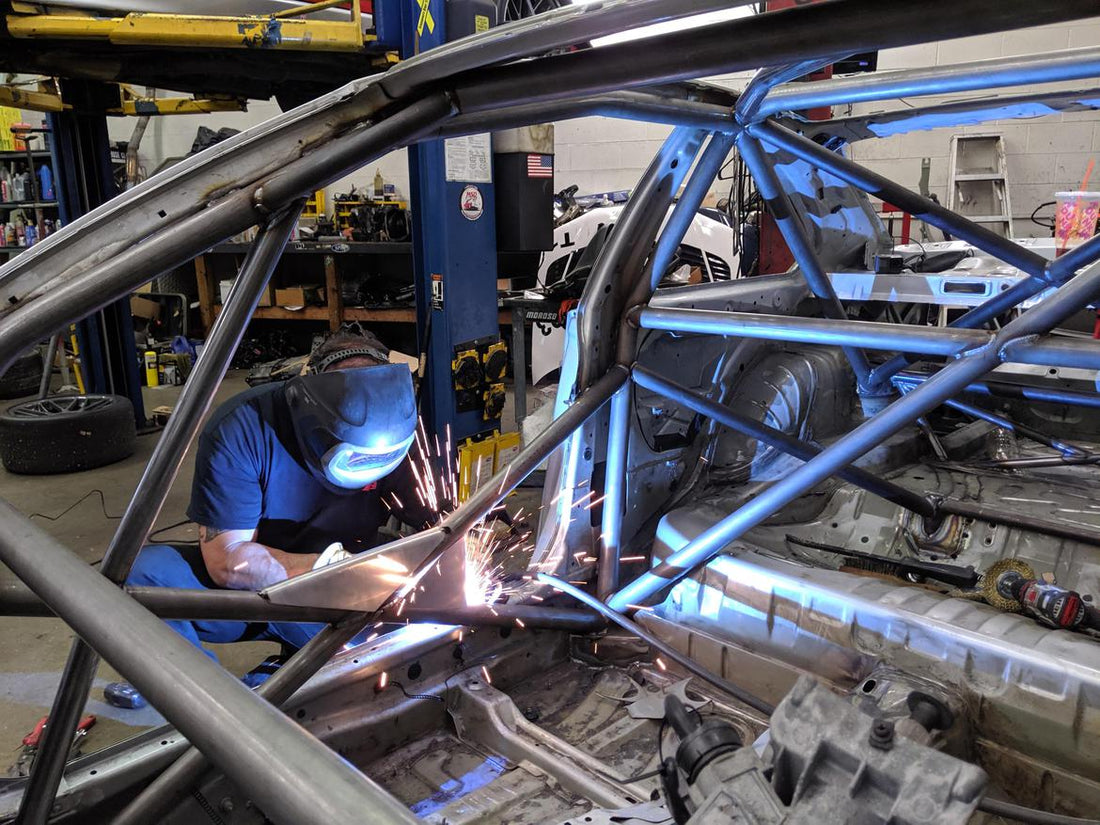 Professional fabricator welding a steel roll cage inside a stripped race car