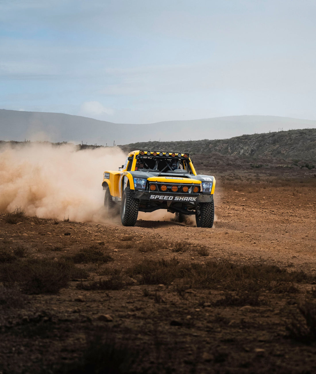 Trophy truck racing through the Baja desert in a cloud of dust