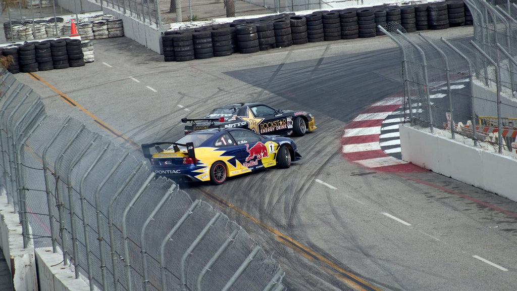 Two drift cars slide through a fenced corner at a Formula Drift event in April 2006.