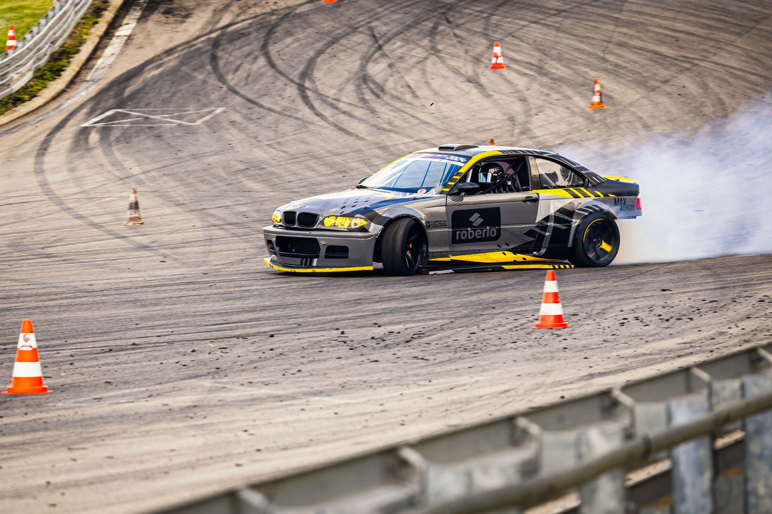A gray and yellow BMW drift car with a helmeted driver, countersteered front wheels and rear-tire smoke.