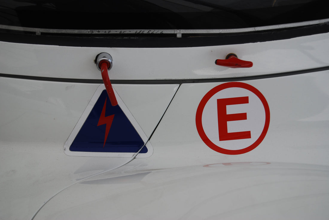 Two external red controls on a Porsche race car, one marked for electrical cutoff and one with the extinguisher E symbol.