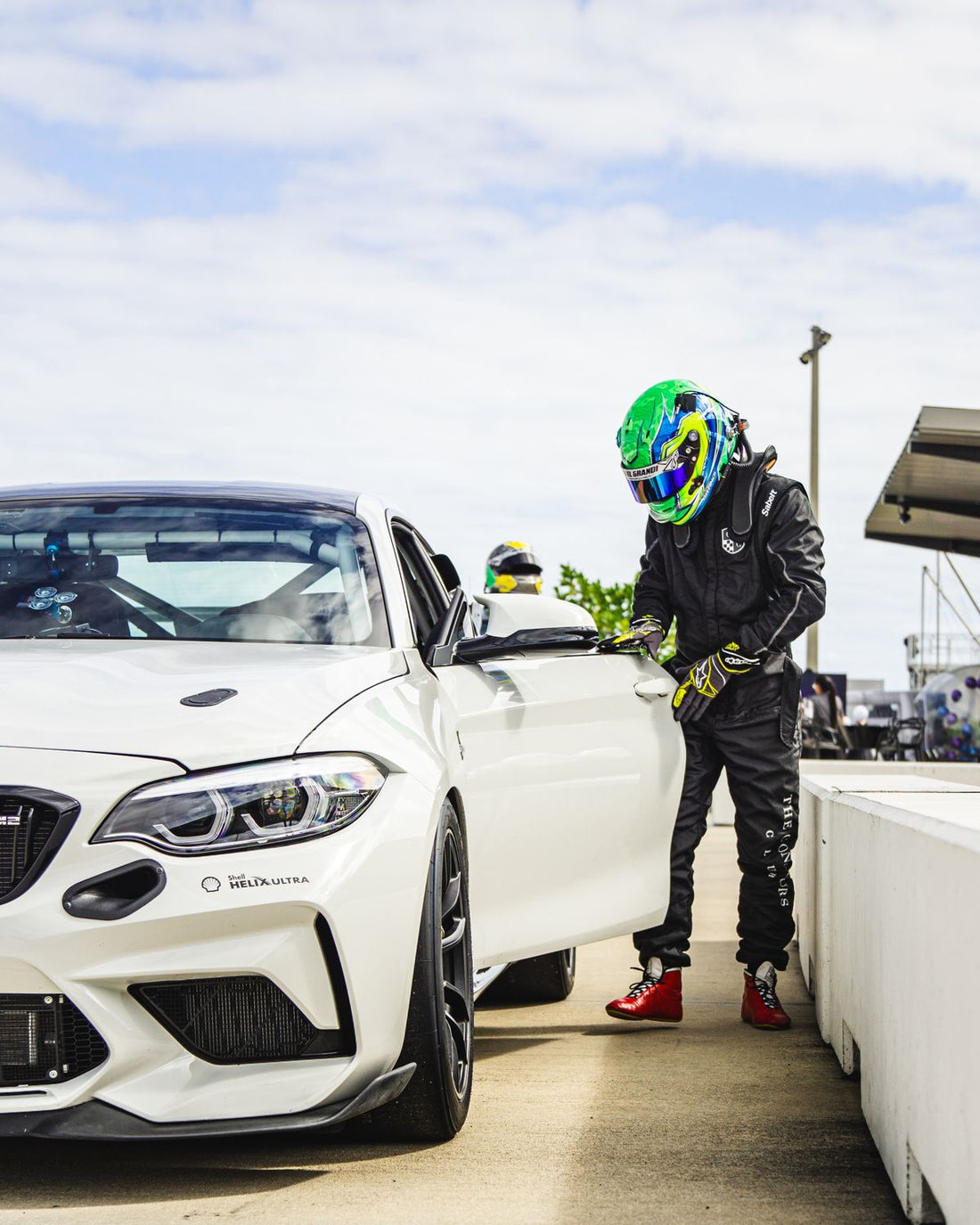 A helmeted driver beside a white car in a pit lane. Representative motorsports photograph; helmet model, condition and certification are not identified.