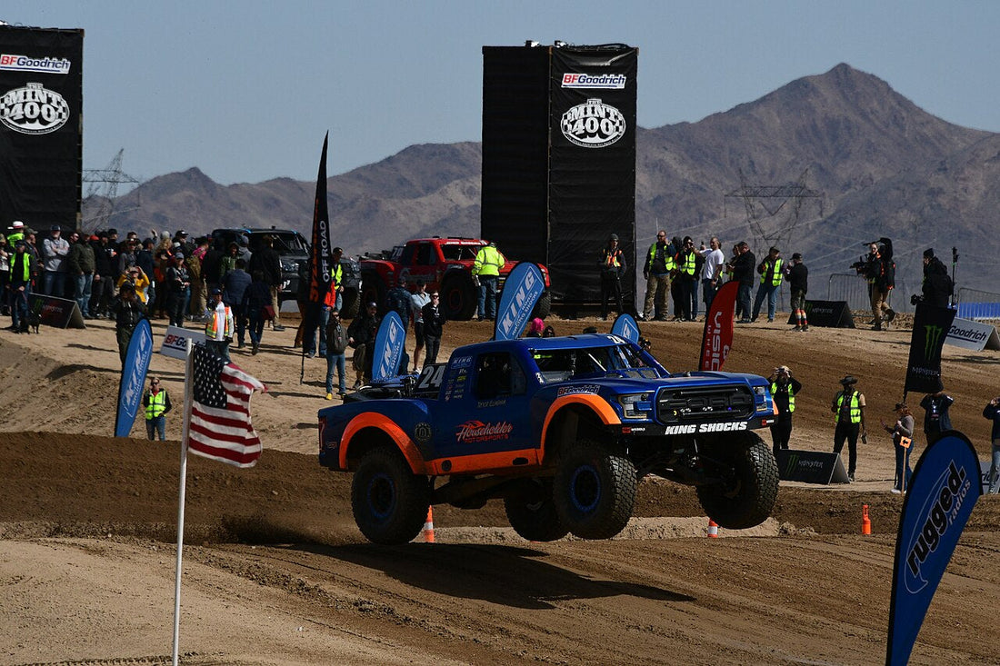 Blue and orange racing truck airborne over a dirt section at the 2024 Mint 400.