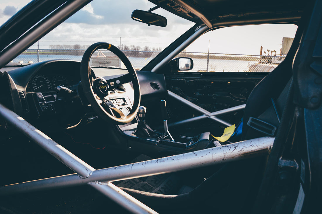 Race car interior showing a welded roll cage and side-impact door bars; archive safety-cage image by Lloyd Dirks, CC0 via Wikimedia Commons.